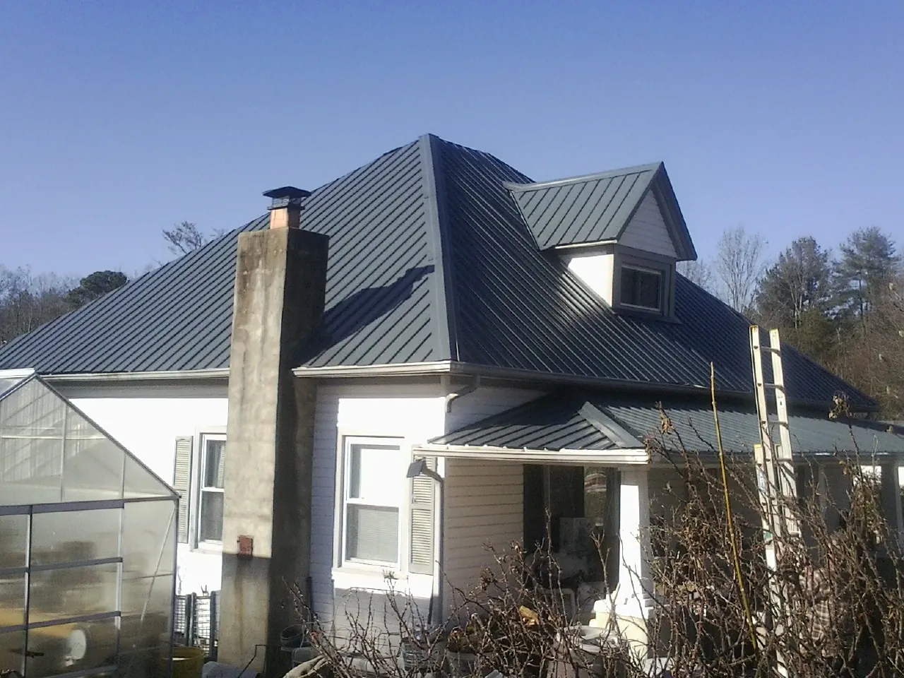 Dark blue standing seam metal roof on a white farmhouse with dormer — Slate & Tile Roof Repair by Roofing Brothers in Levan