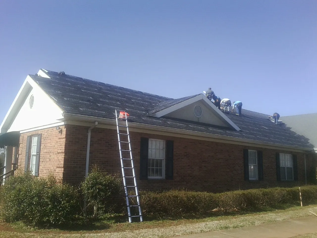 Crew tearing shingles off a brick ranch roof with a ladder set — Metal Roof Repair work by our crew in Levan