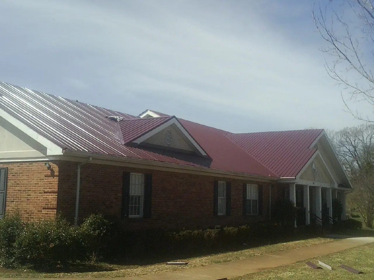Red metal roof with gabled entries on a long brick building, from a Hail Damage Roof Repair job in Levan