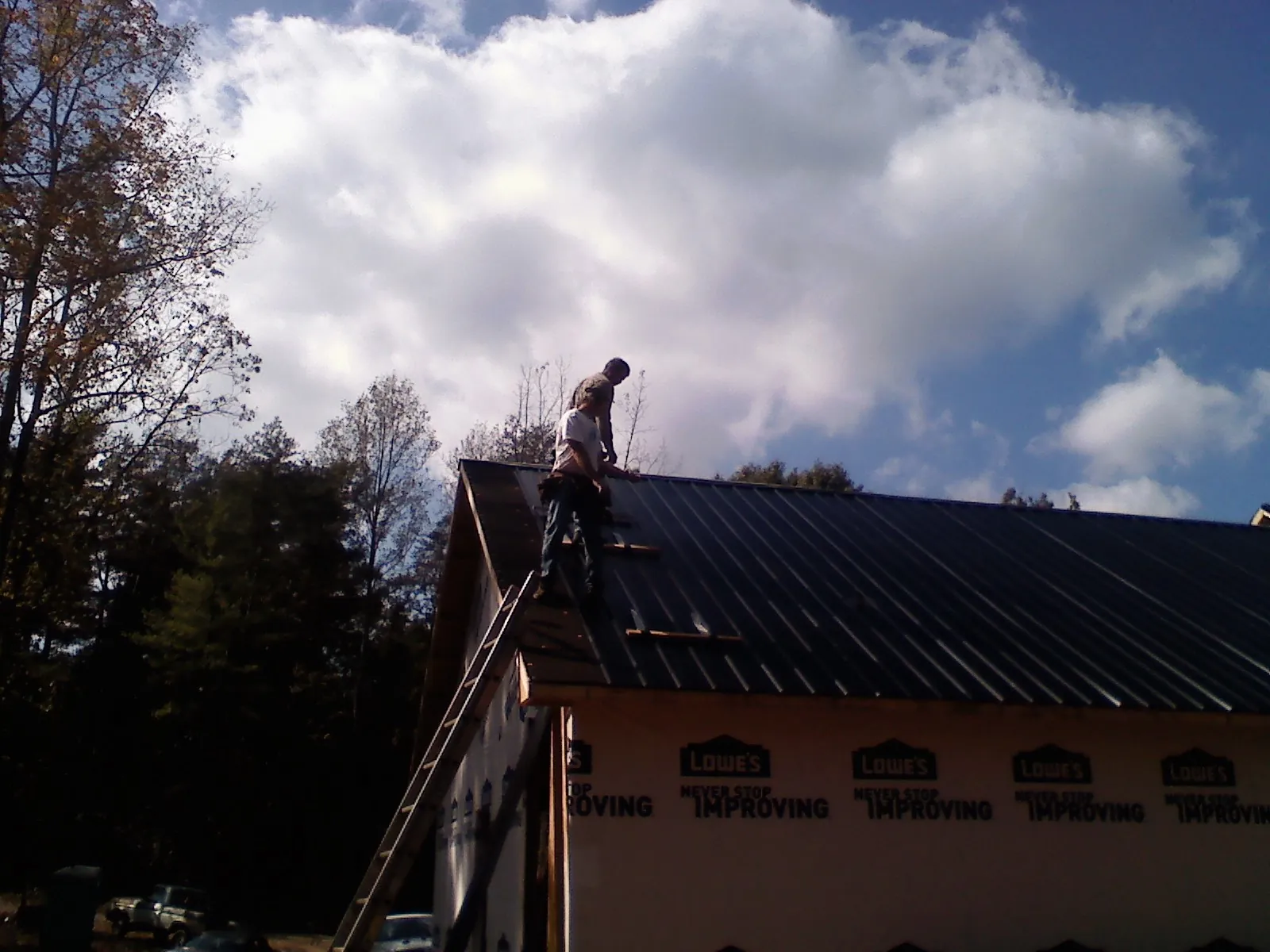 Roofer fastening dark metal panels high against a cloudy sky, from a Roof Inspection job in Levan